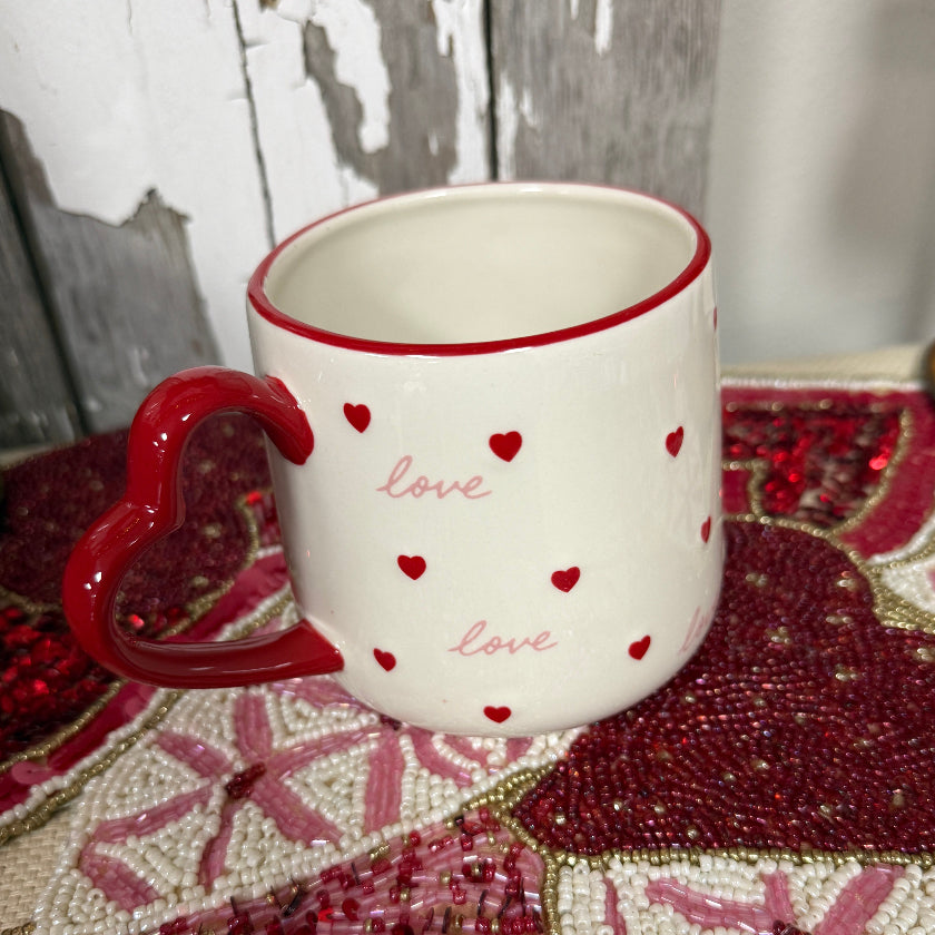 White mug with red hearts and 'love' text on a decorative surface with pink and red patterns.