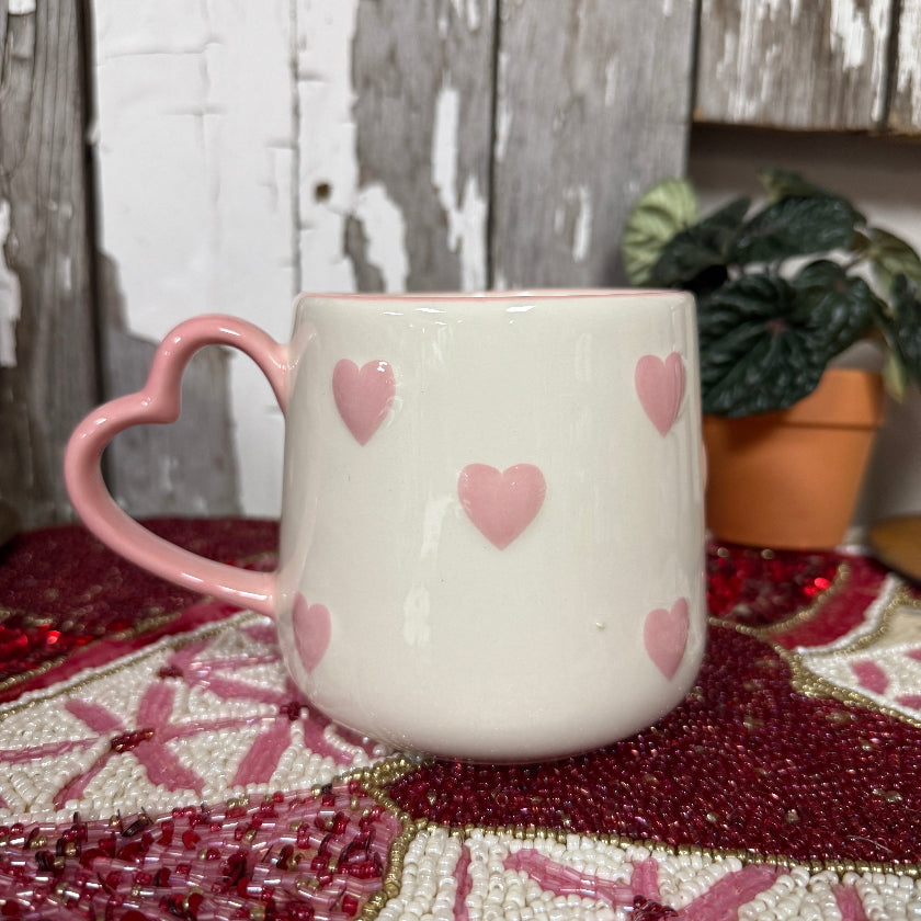 White mug with pink hearts on a decorative surface with a wooden background