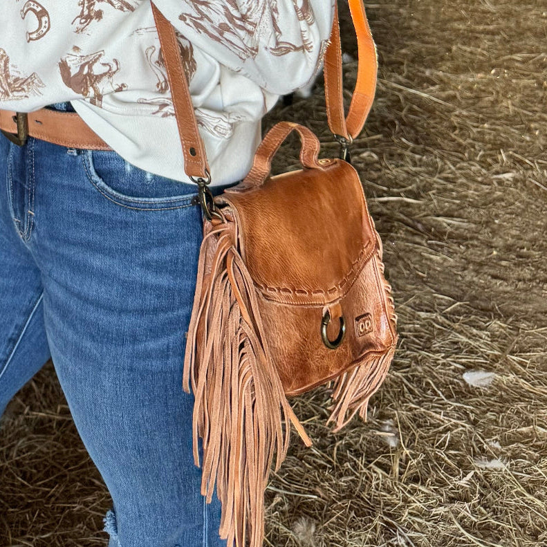 Person wearing a brown leather bag with fringes on a hay background