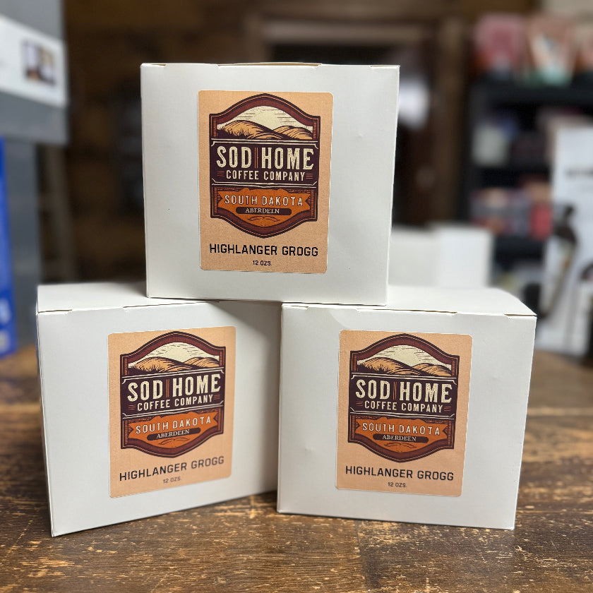 Three boxes of Sod Home Coffee Company Highlander Grogg on a wooden surface.