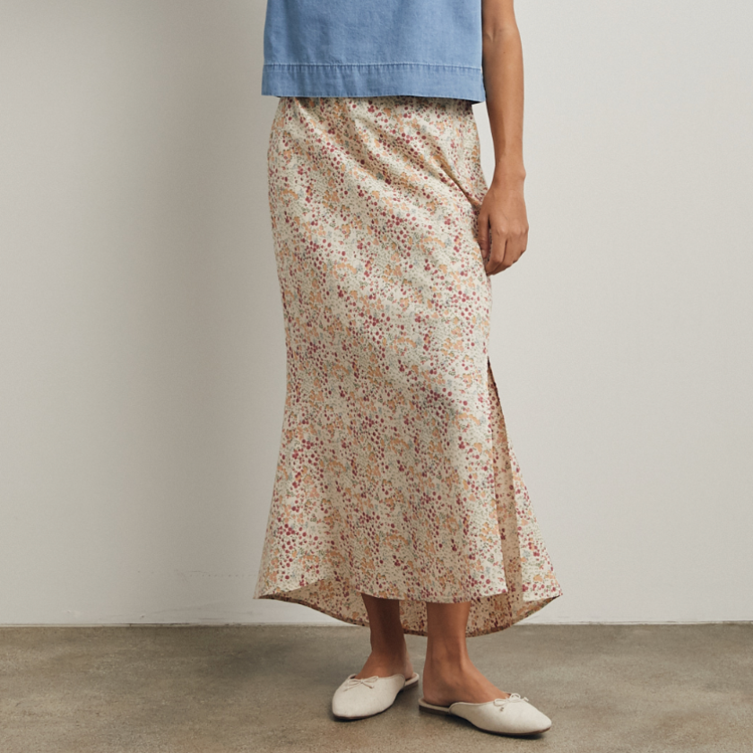 Woman wearing a blue sleeveless top and floral skirt against a plain background