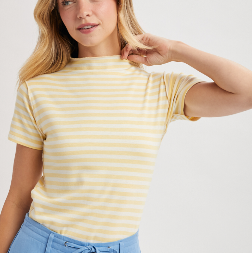 Woman wearing a yellow and white striped shirt with blue pants on a plain background