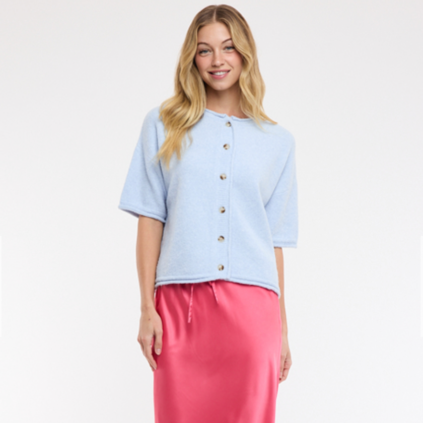 Woman wearing a light blue top with gold buttons and a pink skirt on a white background