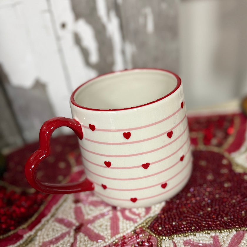 White mug with red heart patterns on a decorative surface with pink and red patterns.