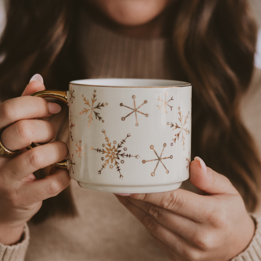 Person holding a mug with snowflake patterns, wearing a brown sweater.