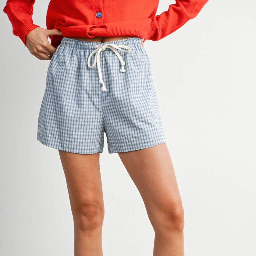Person wearing blue checkered shorts with a red jacket on a plain background