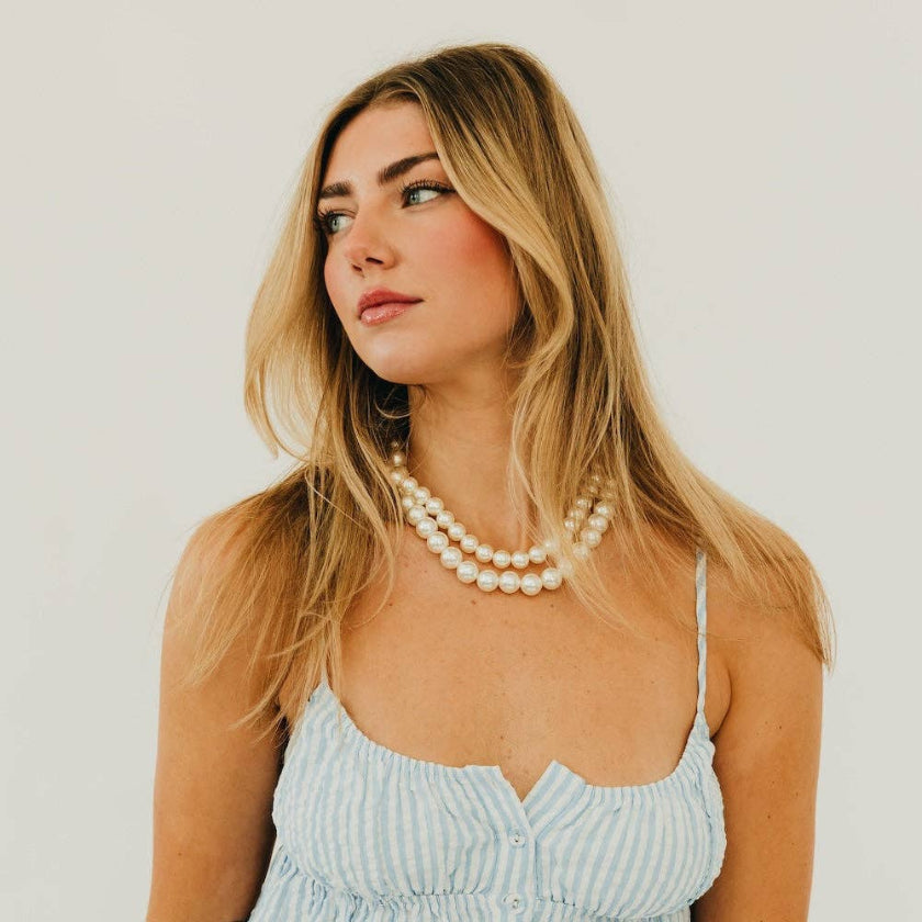 Woman wearing a light blue dress and pearl necklace against a plain background