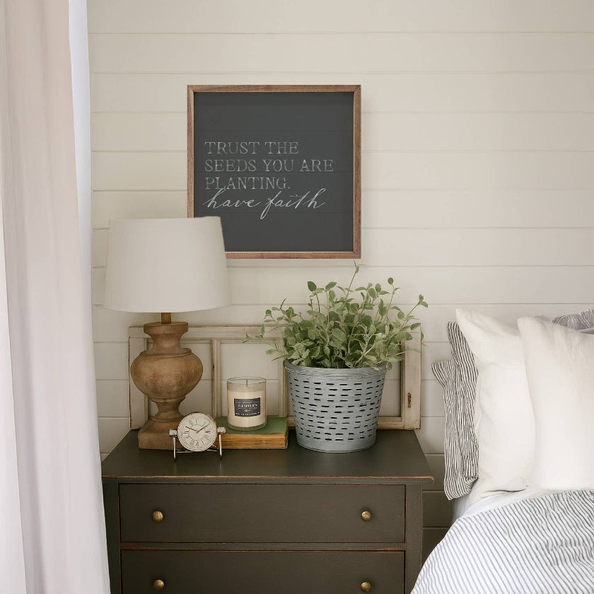 Nursery room with wooden nightstand, lamp, and decorative items against a white paneled wall.