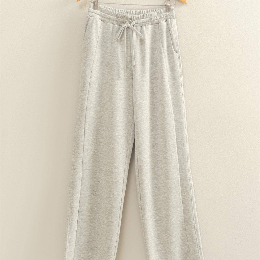 Light gray pants on a wooden hanger against a beige background