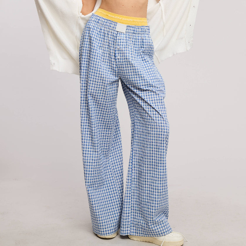 Woman wearing a white top and blue checkered pants holding a white cardigan.