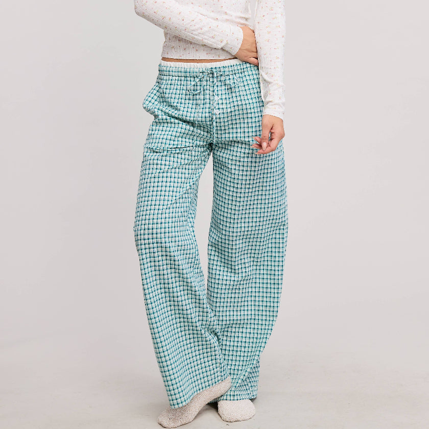 Woman wearing a white long-sleeve top and green checkered pants on a plain background