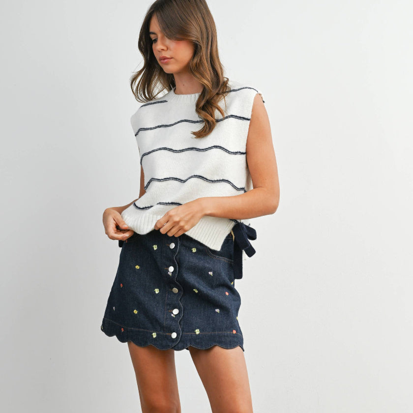 Woman wearing a striped top, navy denim skirt, and black rain boots on a plain background