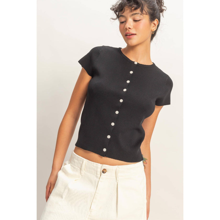 Woman wearing a black short-sleeve button-up top with white pants on a light background