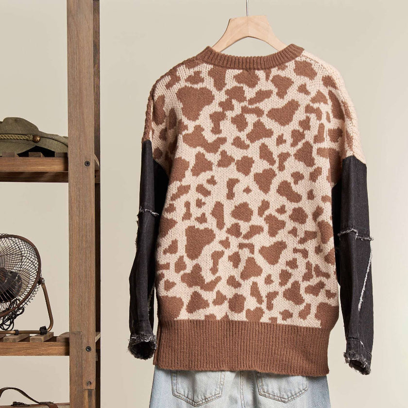 Leopard print sweater with brown and black sleeves on a hanger against a neutral background.