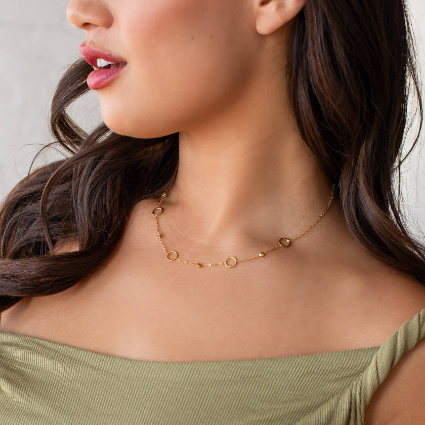 Close-up of a woman wearing a delicate gold necklace with a neutral background