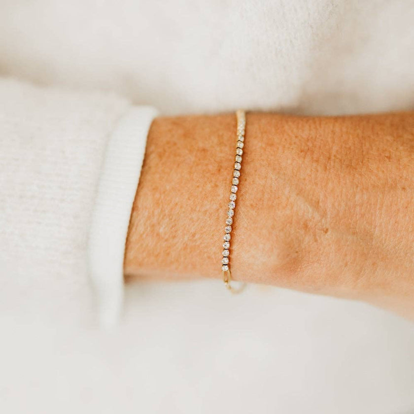 Close-up of a person's wrist wearing a delicate gold bracelet on a light background