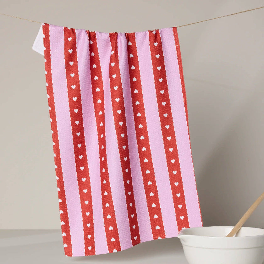 Red and pink striped towel with heart patterns hanging on a line, next to a white bowl.