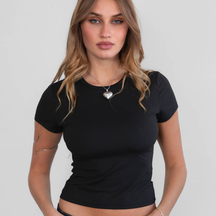 Woman wearing a black t-shirt and dark jeans against a plain background