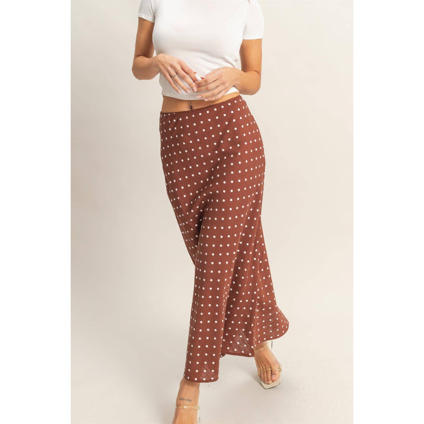 Person wearing brown polka dot pants and a white top on a light background
