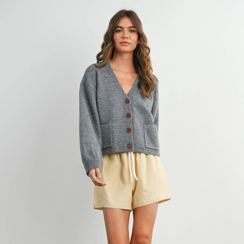 Woman wearing a gray cardigan, yellow shorts, and white socks against a plain background