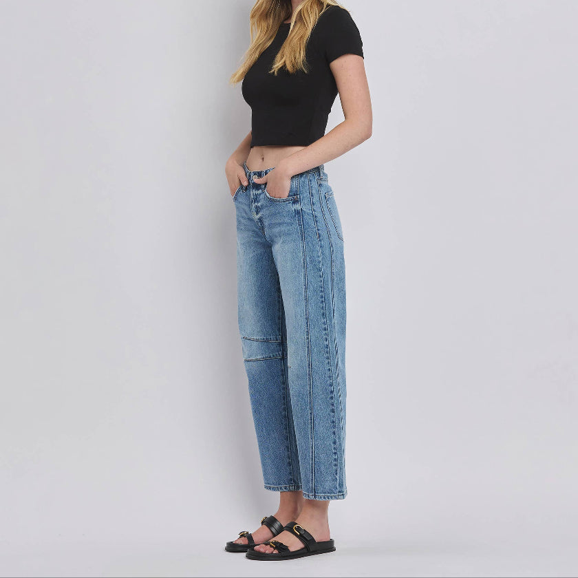 Woman wearing a black top and blue jeans against a plain background