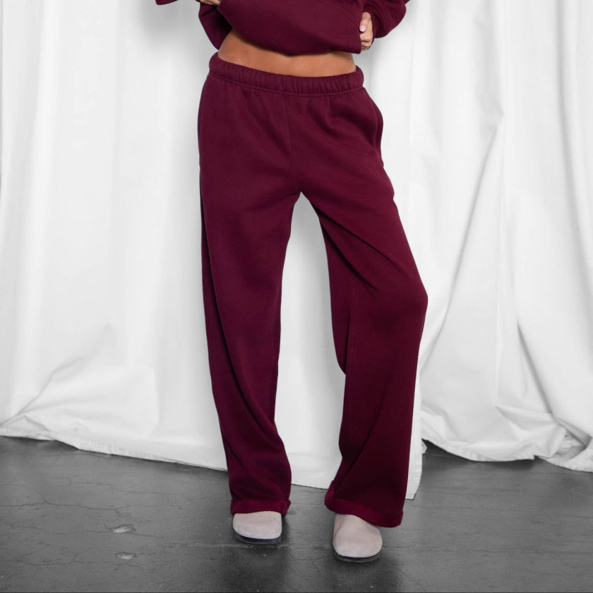 Woman wearing a burgundy tracksuit against a white curtain background