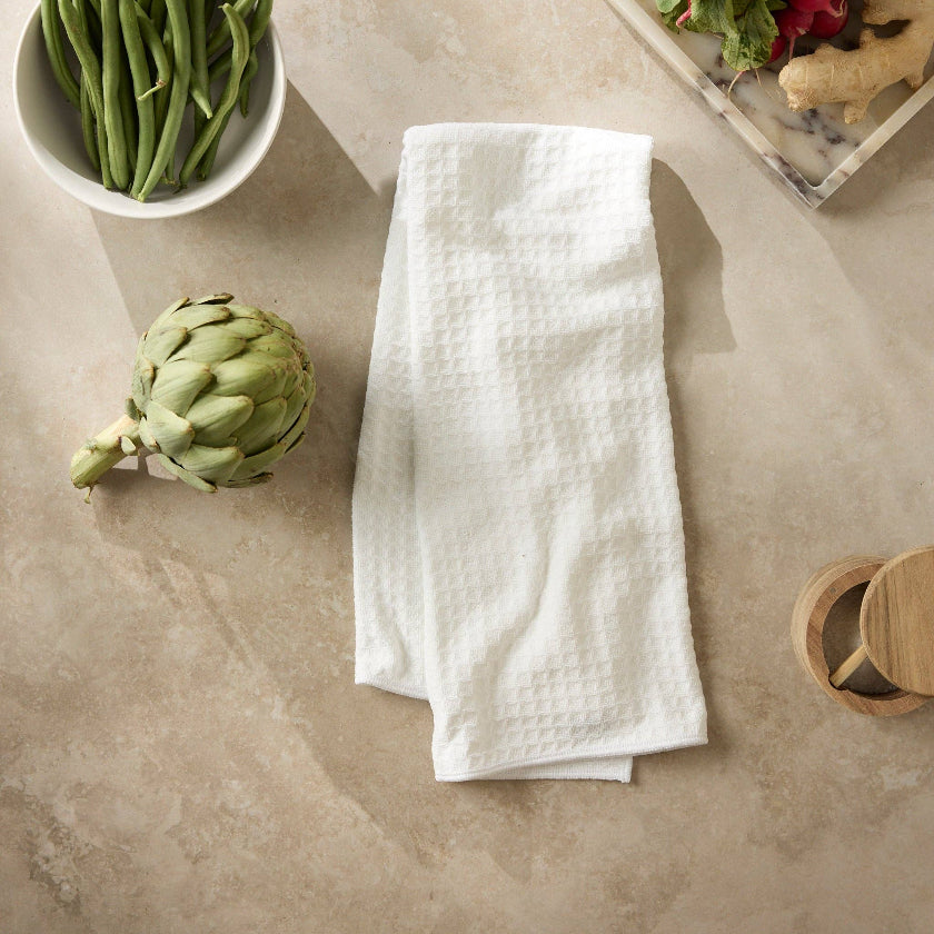 White kitchen towel on a beige surface with green beans, artichoke, and salad.