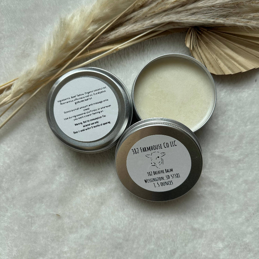 Two metal tins with balms on a light gray surface with dried leaves.