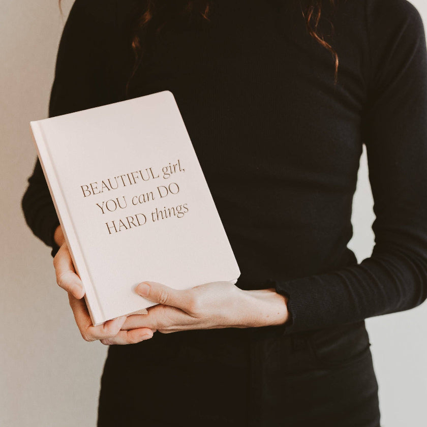 Person holding a book titled 'Beautiful girl, YOU can DO HARD things' against a neutral background
