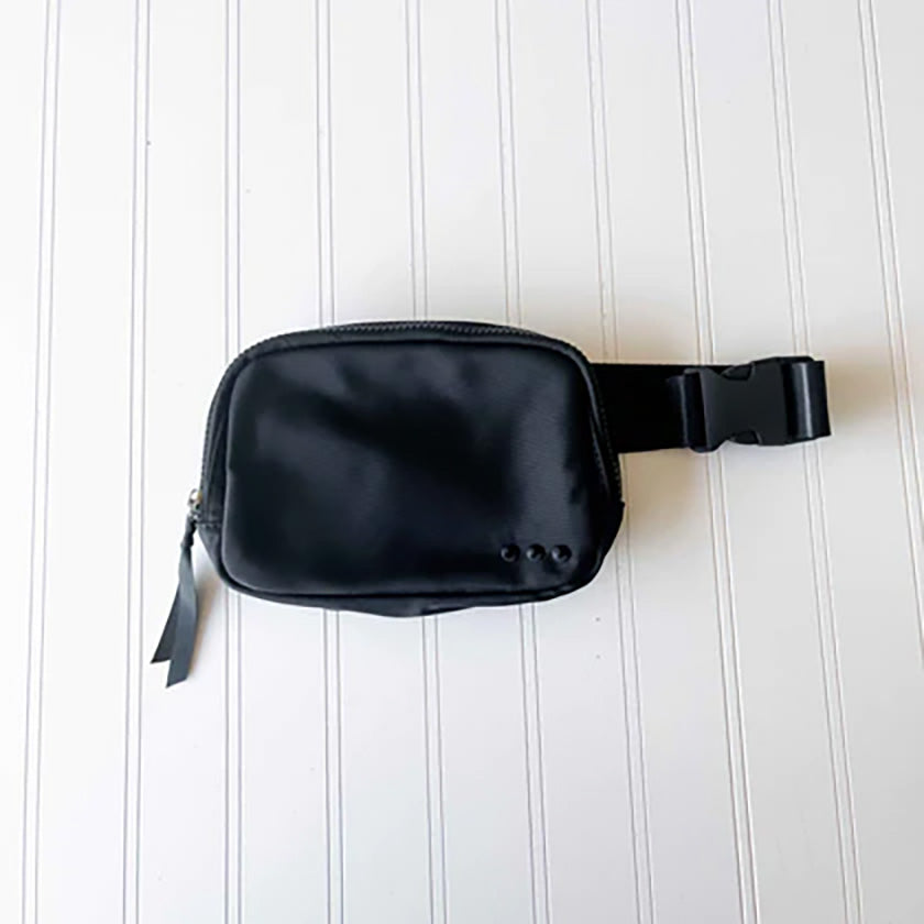 The Nadya Nylon Bum Bag in Black includes a main zipper, a chevron interior, an interior zipper pocket, and an adjustable buckle strap. There is also a zippered pocket on the back of the bag for easy-access to your essentials, and ribbon on each of the exterior zippers.
