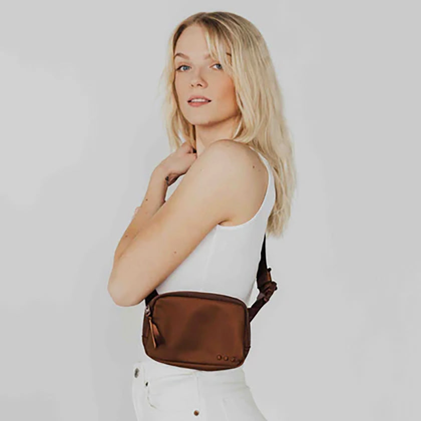 The Nadya Nylon Bum Bag in Brown includes a main zipper, a chevron interior, an interior zipper pocket, and an adjustable buckle strap. There is also a zippered pocket on the back of the bag for easy-access to your essentials, and ribbon on each of the exterior zippers.